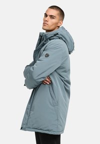 Ljusblå isolerad parka med huva, som har dragkedja framtill, sidofickor och en logotyp på vänster ärm. Slät struktur.