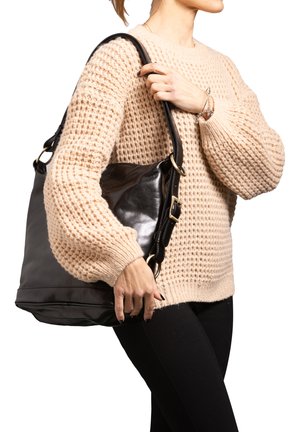 Borsa a spalla in pelle nera con hardware dorato, design spazioso e texture morbida. Indossata con un maglione lavorato a maglia beige e pantaloni neri.