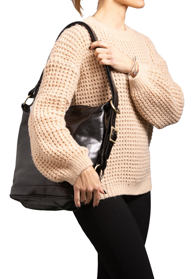 Borsa a spalla in pelle nera con hardware dorato, design spazioso e texture morbida. Indossata con un maglione lavorato a maglia beige e pantaloni neri.
