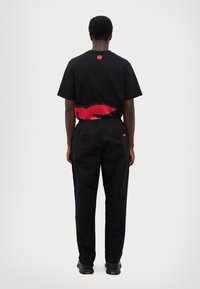 Black cotton t-shirt with a red graphic on the back, paired with black elastic-waist pants. The ensemble features spacious back pockets.
