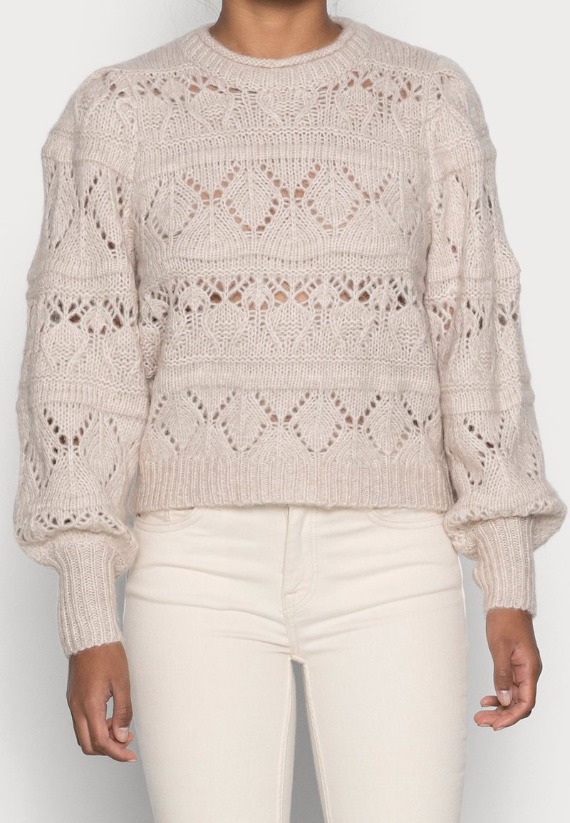 Suéter de punto en beige pálido con intrincados patrones calados. Presenta un cuello redondo y mangas globo con puños y dobladillo acanalados.