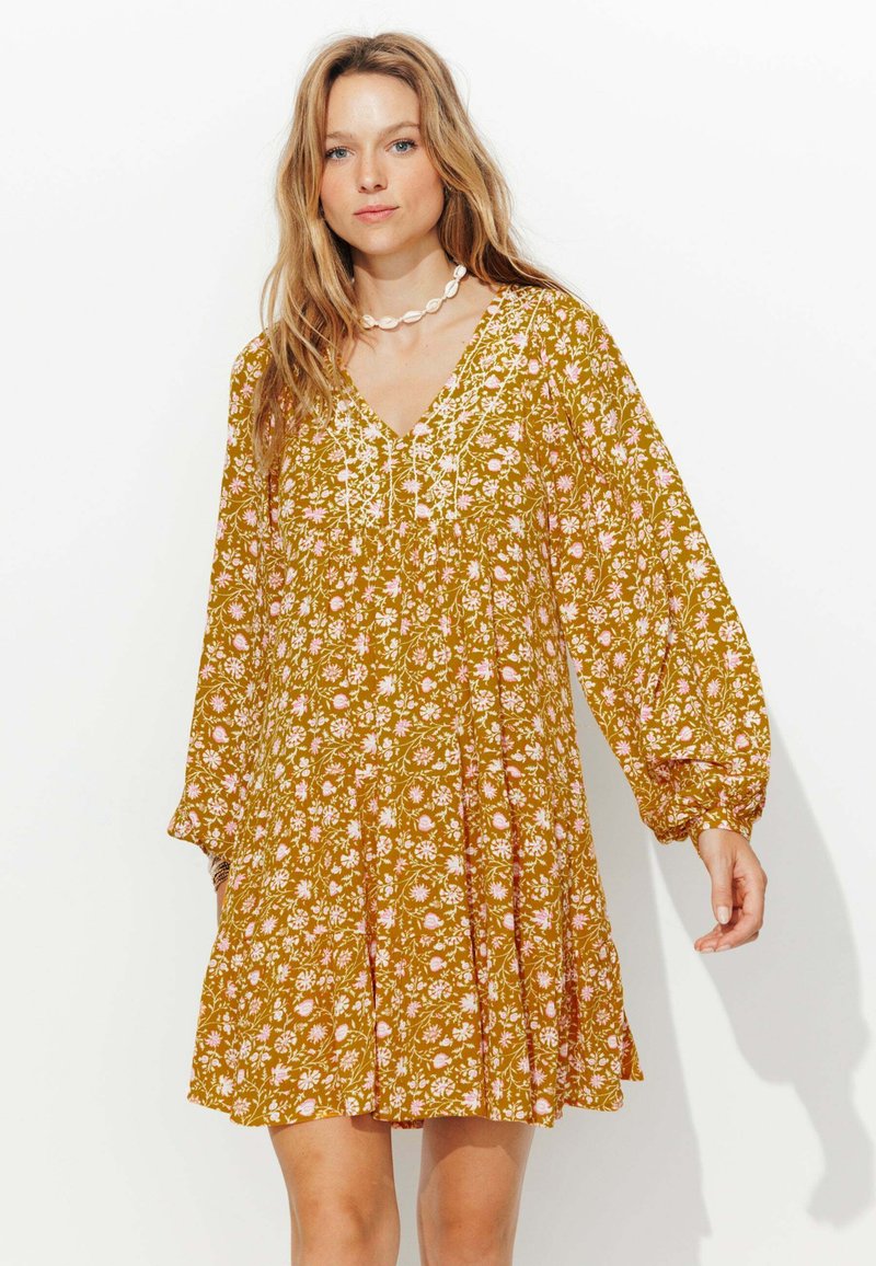 Robe florale jaune moutarde avec de longues manches bouffantes, décolleté en V et détails brodés. Présente une coupe ample et une jupe à volants avec un motif ludique.