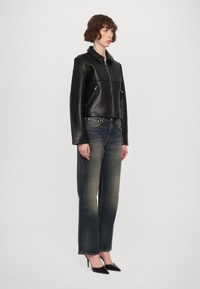 Svart lädercropped jacka med dragkedja, två sidofickor, matchad med urblekta blå jeans och svarta spetsiga klackar. Modell står rakt upp.