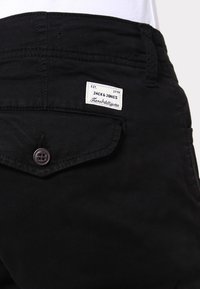 Svarta bomullsbukser med en bakficka med knappstängning och en etikett som säger "JACK & JONES" med etableringsåret 1990.