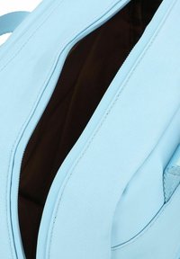 Zaino azzurro chiaro con chiusura a zip, caratterizzato da un'esterno testurizzato e una fodera interna di un marrone scuro. Dettagli di cucitura accentuati visibili.