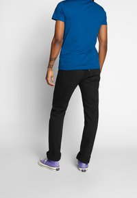 Blå kortärmad t-shirt, svarta slim-fit jeans och lila låga sneakers. Enkelt design med upprullade ärmar och kontrasterande färger.
