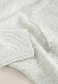 Light gray sweater made of soft knit fabric. Features a pocket, ribbed cuffs, and a smooth texture with subtle variation in color.