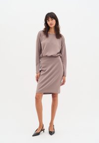 Halenka s dlouhým rukávem v barvě mauve spárovaná s přiléhavou sukní ke kolenům. Hladká tkanina s mírným leskem. Celkový vzhled dotvářejí černé lodičky s špičkou.