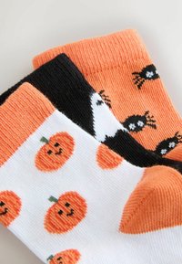 Drei Paare Baumwollsocken: orange mit schwarzen Spinnen, weiß mit orangefarbigen Kürbissen und schwarz mit weißen Akzenten. Strukturierte Strickbündchen.