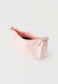 Lyst rosa stoff midjeveske med en toppglidelås som er delvis åpen, rektangulært logo-patch på forsiden, og justerbar stropp med spenne på siden.