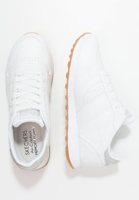 Baskets de sport blanches avec une tige en cuir lisse, des accents en argent texturé sur le talon et une semelle en caoutchouc gomme. Elles sont dotées de lacets traditionnels.