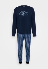 Camiseta azul marino de manga larga con el logo del cocodrilo de Lacoste en color blanco, combinada con pantalones de pijama azules con estampado de logotipos repetidos y puños acanalados.
