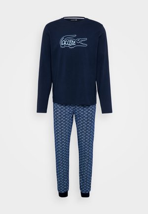 Granatowa koszulka z długim rękawem z białym logo krokodyla Lacoste, połączona z niebieskimi spodenkami do piżamy z wzorem powtarzających się logo i prążkowanymi mankietami.