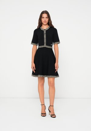 Black dress with short sleeves, textured trim, button closure, and flared skirt. Features contrasting lace-like accents on edges.