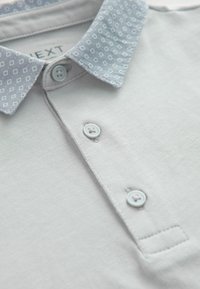 Hele hall polo särgid, millel on mustriline sinine krae, kaks sinist nööpi ja korralik õmblusest detail. Sile kangas tekstuur, millel on peen sära.