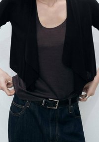 Svart öppen cardigan över en mörkgrå tanktop, matchad med mörka denimjeans och ett svart bälte med en metallspänne.