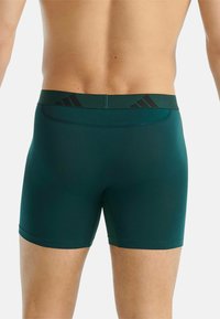 Donkergroene boxershorts voor mannen met een zwarte tailleband waarop het Adidas-logo staat. Rekbare stof met een gladde textuur.