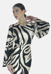 Robe en satin noir et crème avec un motif abstrait audacieux, des manches longues en cloche et un col rond. Texture lisse et design ajusté.