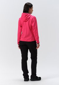 Fuchsia Softshelljacke mit Kapuze, taillierter Schnitt. Kombiniert mit schwarzen Hosen und schwarzem Schuhwerk. Glatte Textur, keine Muster oder Akzente.