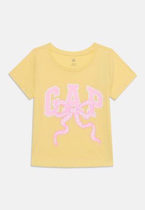 Κίτρινο κοντομάνικο μπλουζάκι με ροζ γράμματα "GAP" και μεγάλο ροζ φιόγκο στο μπροστινό μέρος.
