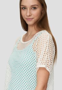 Witte mesh top met een ronde halslijn, voorzien van een blauwe onderlaag. Het mesh ontwerp heeft een rasterpatroon en korte mouwen.