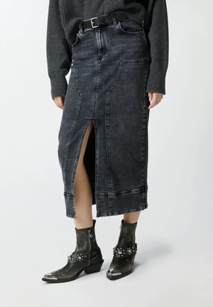Falda midi de mezclilla oscura con una abertura frontal, costuras en contraste y cintura con cinturón. Combinada con botines negros hasta el tobillo con acentos metálicos.