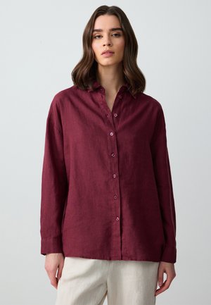 Camicia in lino bordeaux con maniche lunghe e colletto, dotata di bottoni coordinati e una vestibilità rilassata. Texture morbida e leggero lucido.