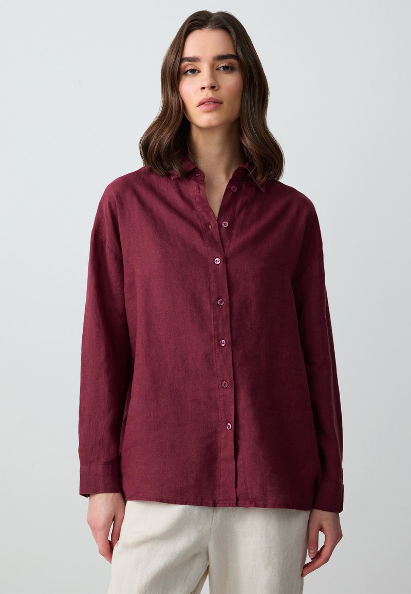 Camicia in lino bordeaux con maniche lunghe e colletto, dotata di bottoni coordinati e una vestibilità rilassata. Texture morbida e leggero lucido.