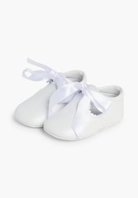 Zapatos de bebé de piel blanca con bordes ondulados y anchas cintas de satén blancas atadas en forma de lazo en la parte delantera. Textura suave, diseño de punta redonda.