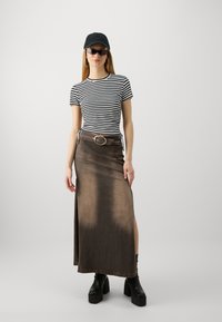 Svart og hvit stripete t-skjorte, brun denim maxiskjørt med sidesplit, sølvbelte, svart caps, store solbriller, kraftige svarte støvler.