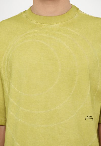 Short-sleeve, bright yellow t-shirt made of soft fabric featuring circular stitching patterns and a small black logo on the lower right.