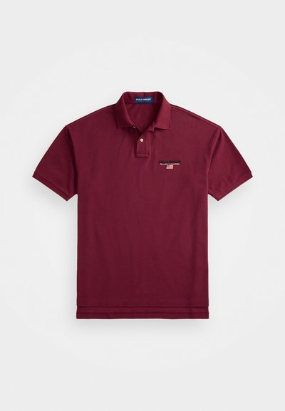 Polo de cor berinjela feito de algodão, com colarinho clássico, pala com dois botões e um pequeno logo bordado no peito.