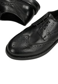 Černé kožené brogue boty s dekorativními perforacemi, hladkou texturou, zaoblenou špičkou a elegantním, lesklým povrchem. Šněrovací design.