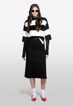 Black denim skirt with side seams, paired with a black and white striped oversized shirt. Accessorized with white sunglasses and red shoes.