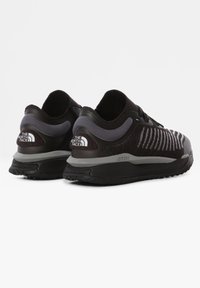 Svarta sportskor med en texturerad stickad ovandel, grå detaljer och en kontrasterande gummisula. Har en logotyp på hälen och reflexområden.