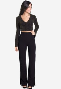 Crop top noir à manches longues avec un décolleté en V et des accents métalliques, associé à un pantalon noir taille haute avec des fentes sur les côtés.