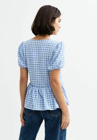 Blå och vit gingham peplum-topp med puffärmar. Mjuk tyg med en texturerad yta och rund halsringning, uppsydd vid midjan.