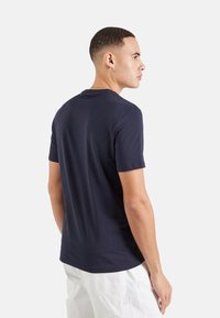 Camiseta de cuello redondo en azul marino hecha de algodón suave, con mangas cortas y un diseño ajustado. Tejido texturizado con costuras mínimas.