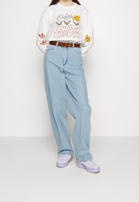 Vit långärmad skjorta med blommönster, kombinerad med ljusblå vida jeans och lavendelplattformsneakers. Brun bälte ingår.