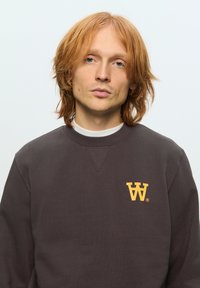 Dark gray sweatshirt featuring a yellow “W” logo on the left chest, made of a textured fabric with a round neckline and long sleeves.