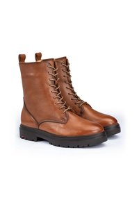 Bottines en cuir marron avec bouts ronds, design à lacets et semelles en caoutchouc robustes. Comprend des boucles sur les côtés et des détails de coutures visibles.