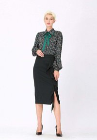 Blouse à motifs floraux avec un nœud vert, associée à une jupe crayon noire avec un avant froncé et une fente sur le côté. Talons hauts noirs.