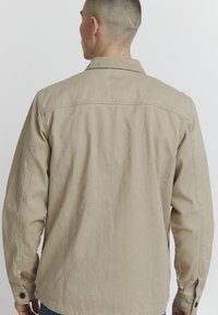 Beige, teksturert bomullsskjorte med lange ermer, knappevrider og krage. Har en rett passform og ryggstropp detalj.