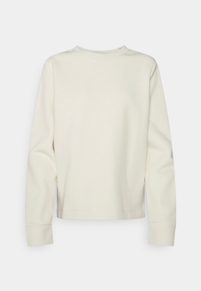 Sudadera de manga larga de color crema claro con cuello redondo, puños acanalados y un logo sutil en la parte delantera. Textura suave, corte cuadrado.