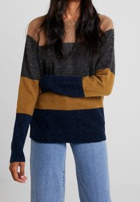 Knit sweater featuring horizontal stripes in brown, gray, mustard, and navy. Loose fit, long sleeves, and textured fabric.