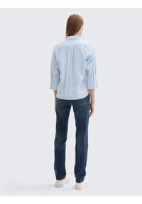 Chemise à rayures bleu clair et blanche avec des manches retroussées, assortie à un jean bleu foncé et des baskets blanches. Design simple et décontracté.