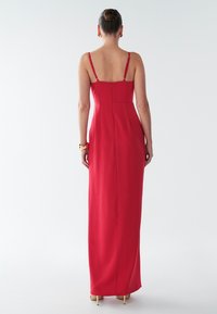 Dlhé červené šaty s tenkými ramienkami, priliehavým živôtikom a rovnou sukňou siahajúcou až po zem. Hladká látka so zipsom na zadnej strane.