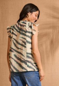 Blusa a maniche corte di colore beige chiaro con strisce astratte nere e verdi, caratterizzata da spalle arricciate e una vestibilità rilassata.