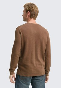 Brauner Langarmpullover aus weichem Material mit Rundhalsausschnitt, gerader Schnitt und gerippten Bündchen, getragen über blauen Denim-Jeans.