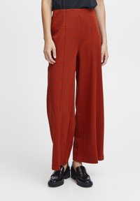 Pantalons à taille haute et jambes larges en motif vichy rouge et noir, présentant un tissu lisse et des plis subtils, accompagnés de mocassins noirs brillants.